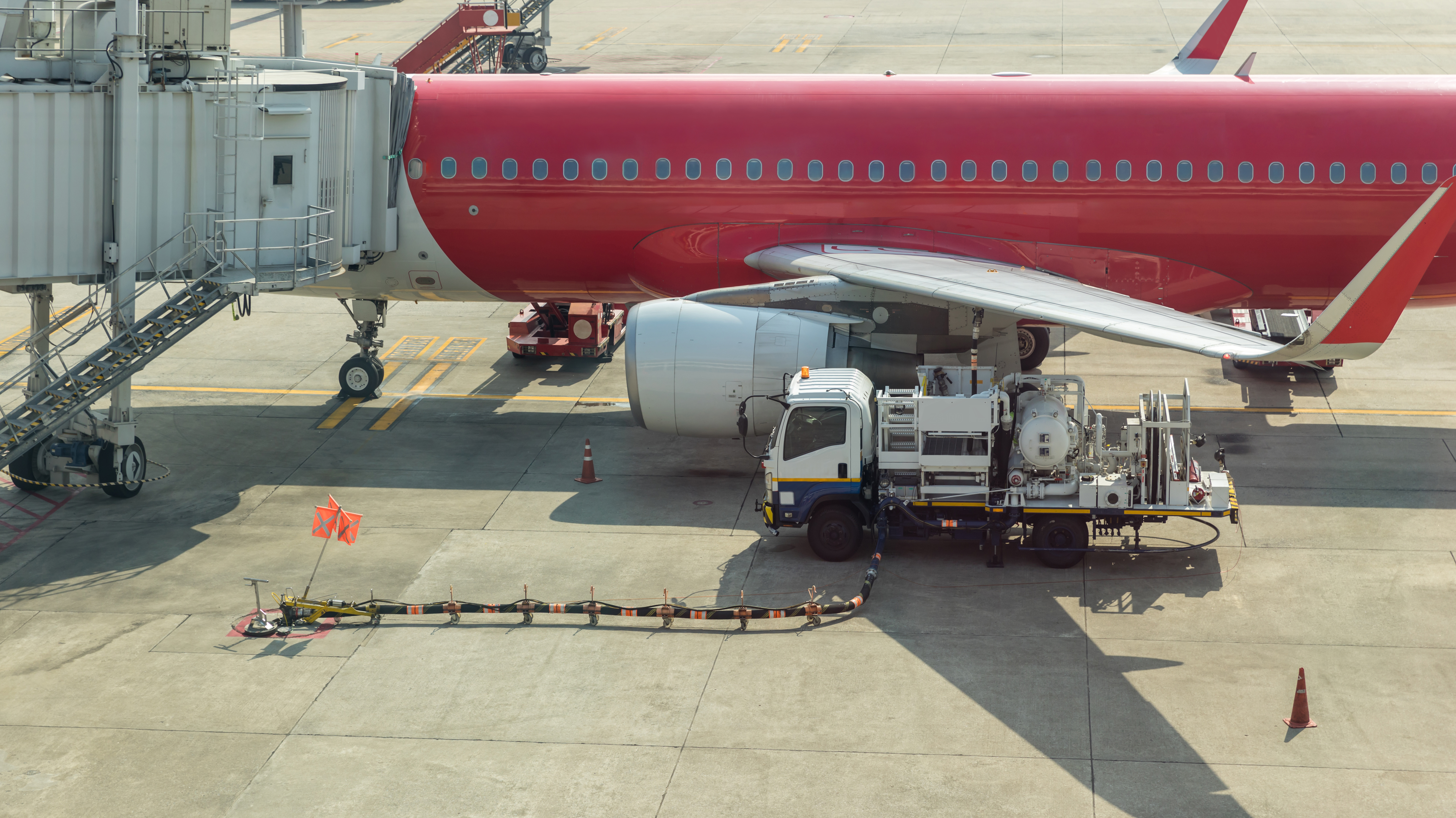 Red commercial airplane refueling at airport gate