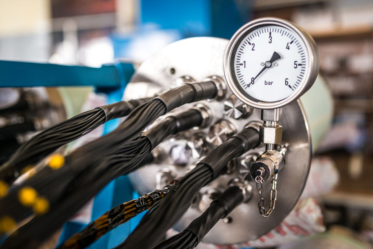 Industrial pressure gauge on metal cylinder with hoses