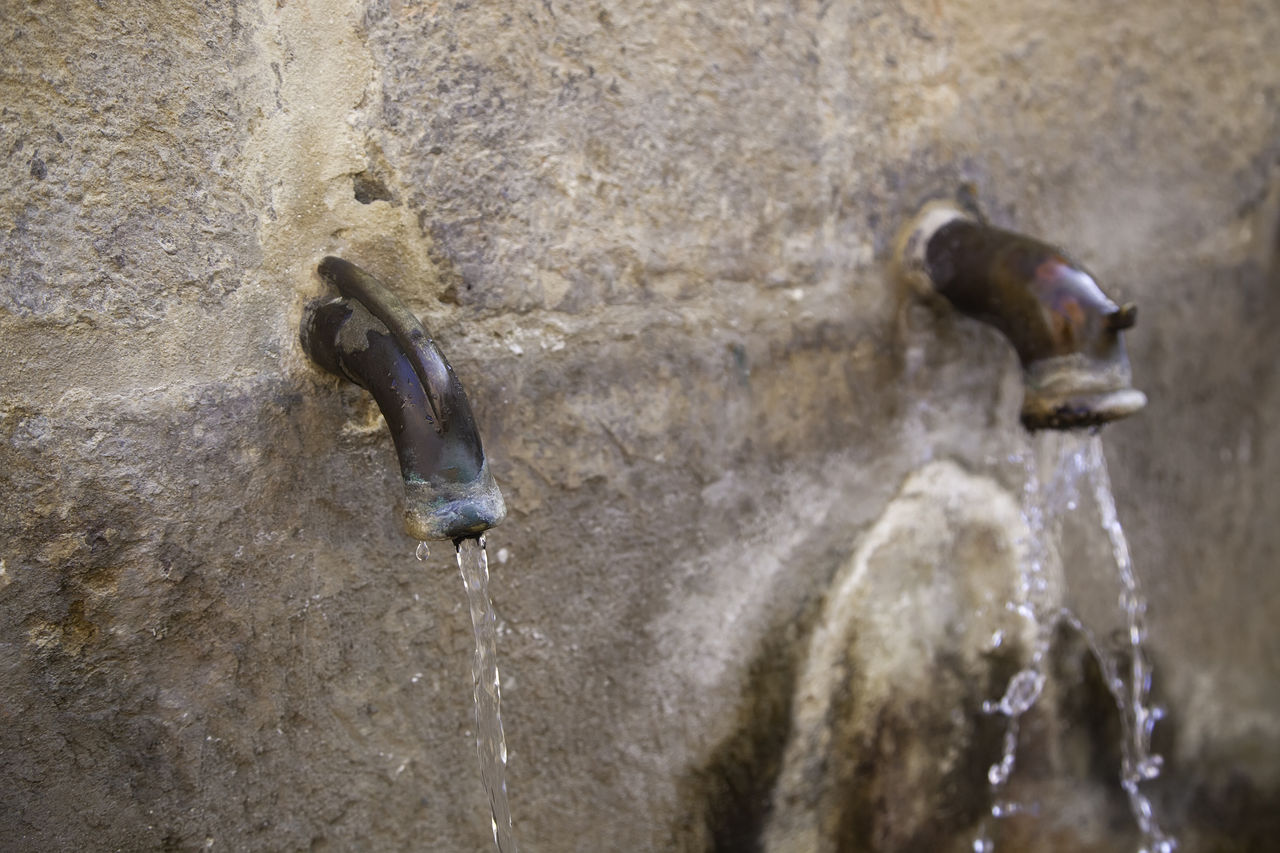 Old metal water taps on stone wall fountain