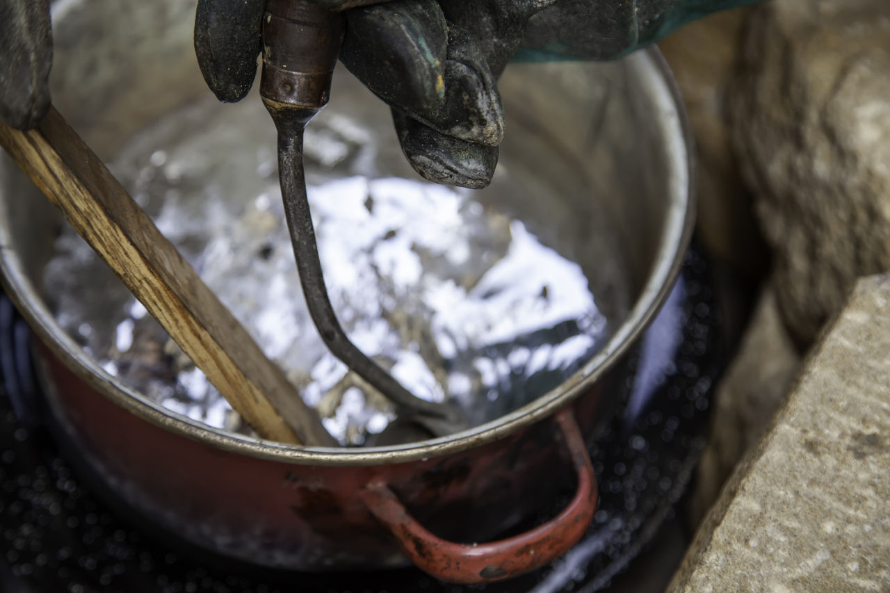 Gloved hand stirring liquid in metal pot outdoors