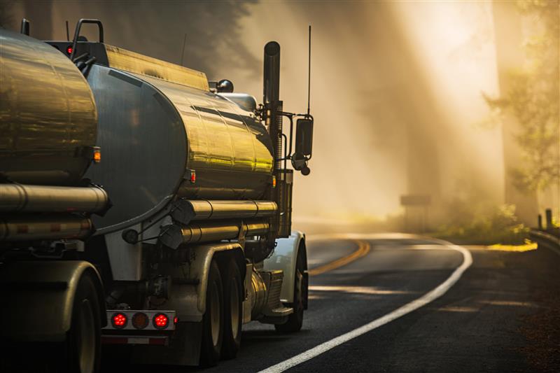 Tanker truck driving on curved forest road at sunrise